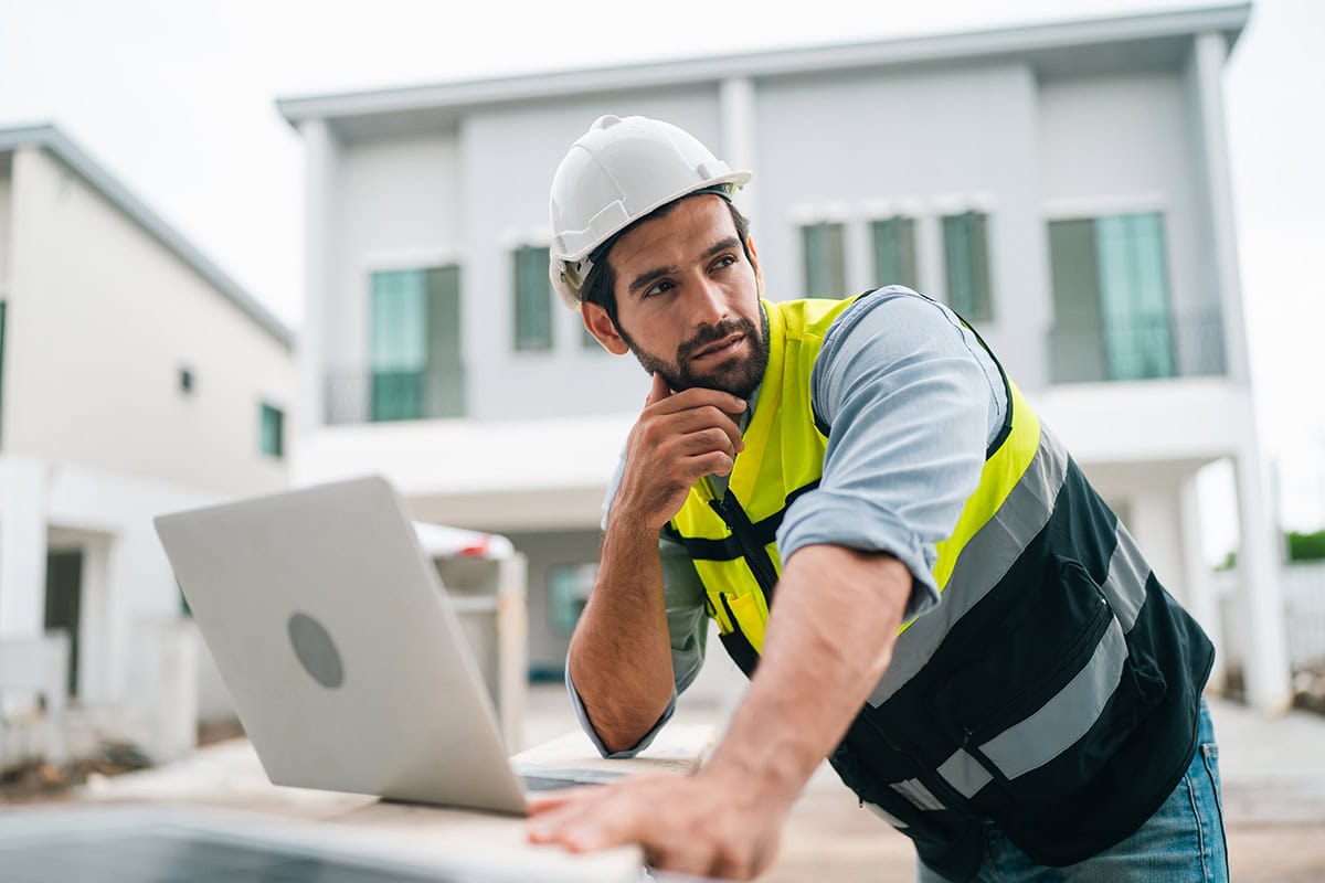 Construction engineer with hard hat working on a laptop at a building site.